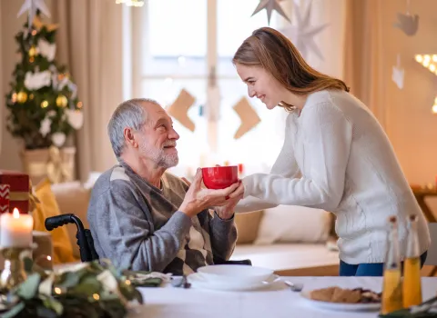 Eine Freiwillige reicht einem älteren Mann eine Tasse Tee.